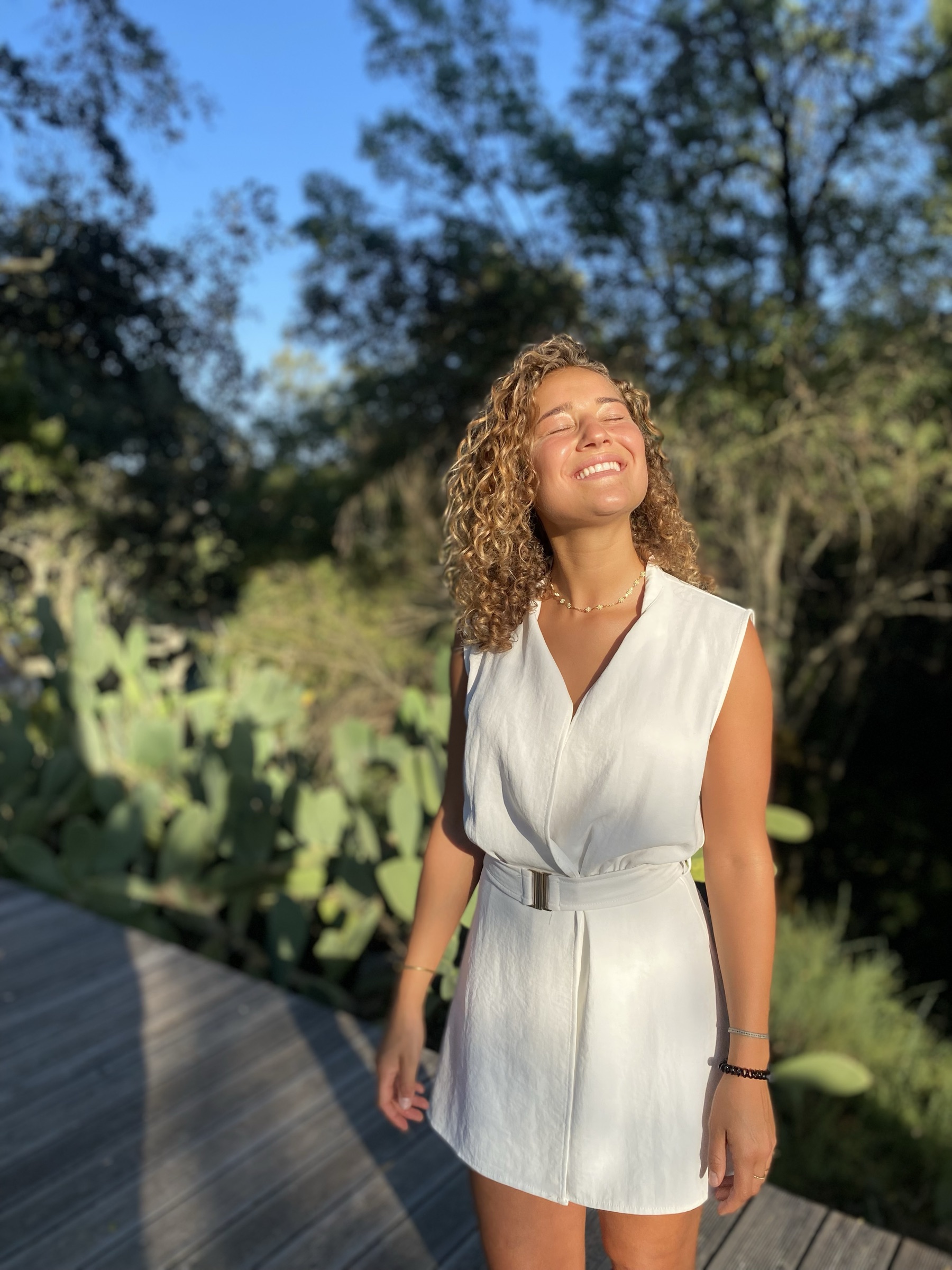 Nina lächelt auf einem Holzsteg in einem grünen Garten der Sonne entgegen